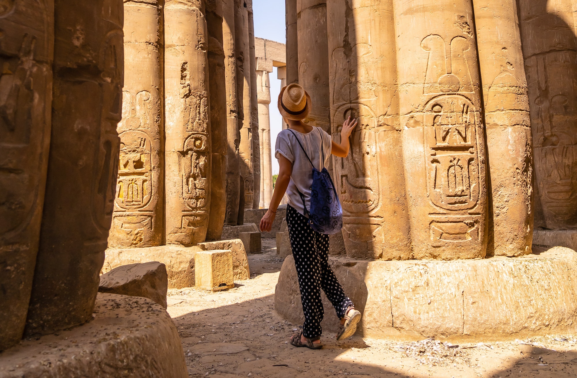 A young tourist in a white t-shirt and hat looking at ancient egyptian, Temple of Luxor, Egypt